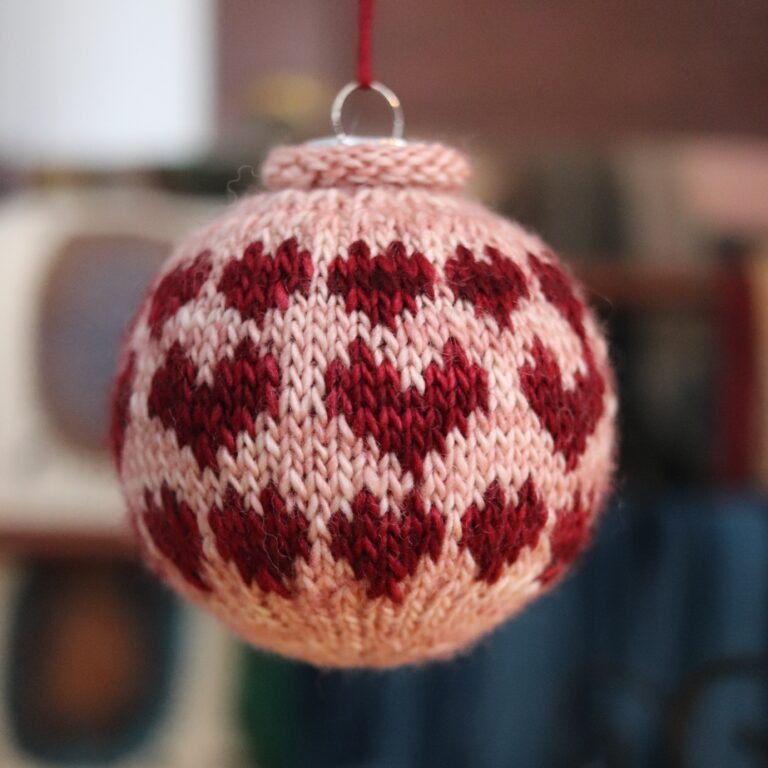 A handknit bauble with red hearts on a pink background